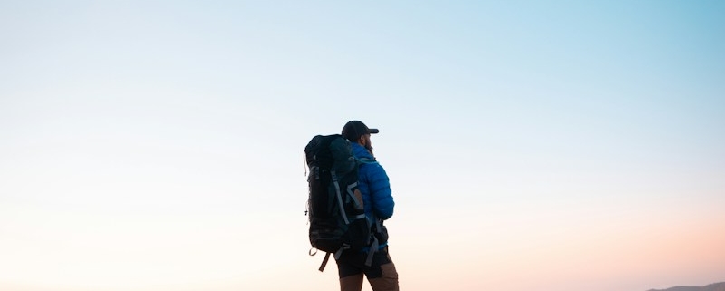 man in black jacket and blue denim shorts with black hiking backpack standing on mountain during