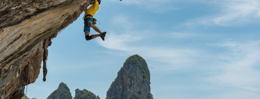 man climbing cliff beside beach